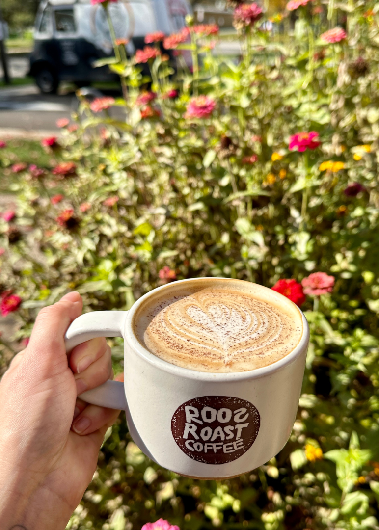 hand holding roosroast mug in garden with latte